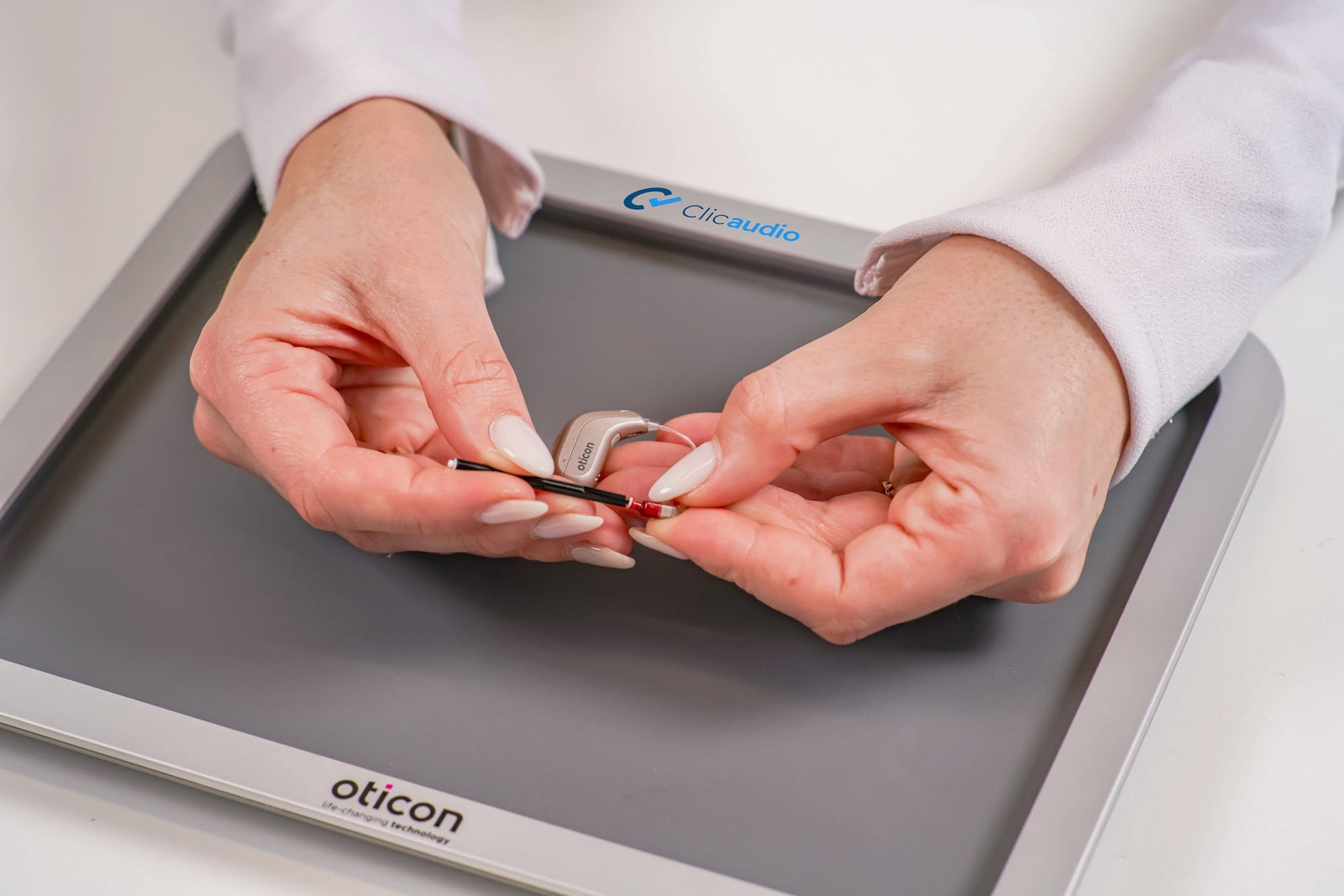 Specialist adjusting an Oticon hearing aid on a Clicaudio fitting tray